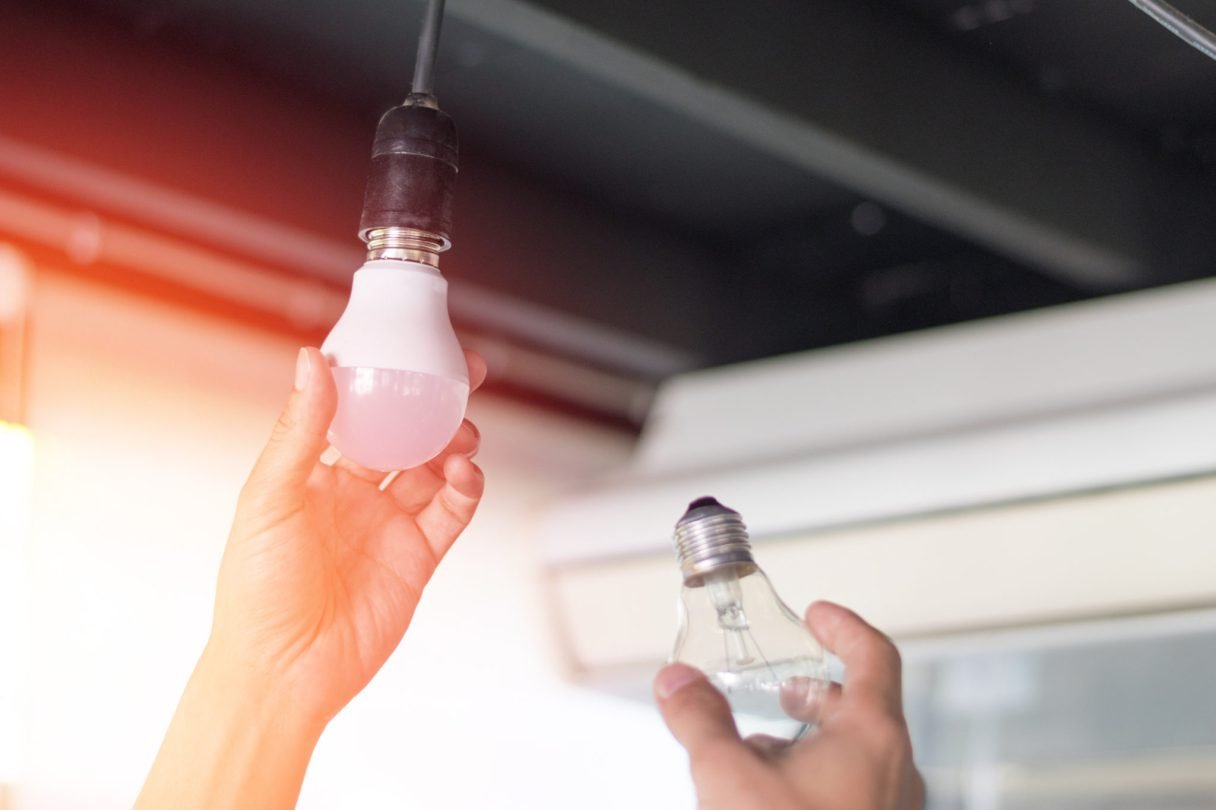 Power saving concept. Asia man changing compact-fluorescent (CFL) bulbs with new LED light bulb. expertos iluminacion led
